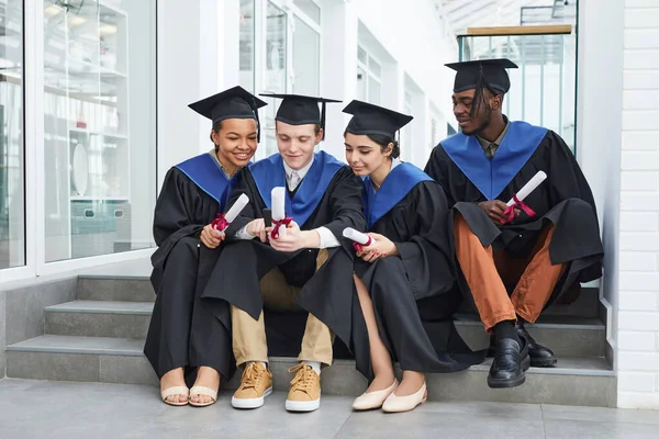 Diverse Groep Gelukkige Jongeren Met Afgestudeerde Jurken Smartphone Terwijl Buiten — Stockfoto