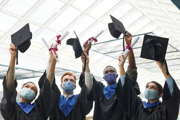 卒業式の間に空気中の帽子を投げ マスクを身に着けている大学卒業生の多様なグループ屋内 コピースペース — ストック写真