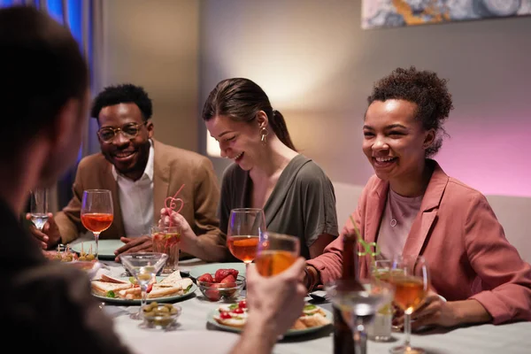 Yemek masasındaki bir grup genç evde eğlenirken mutlu bir şekilde gülüyor.