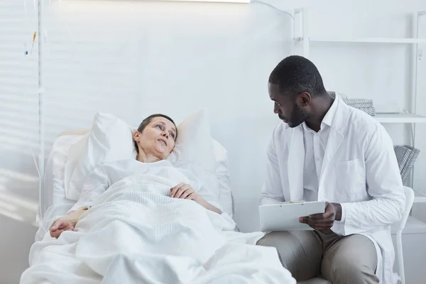 Médico Africano Con Tarjeta Médica Hablando Con Paciente Que Yace —  Fotos de Stock