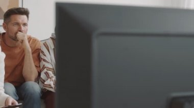 Oturma odasındaki kanepede oturan Afrikalı, Asyalı, Melez Irk ve Kafkasyalı kadın ve erkeklerin televizyon setini geride bırakıp ilginç bir program izliyorlar.