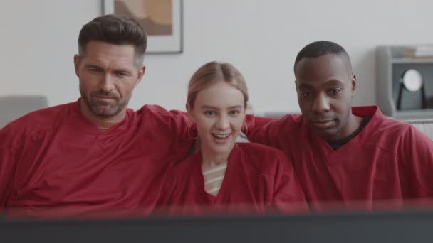 赤い長袖のTシャツを着て 家に座って テレビでゲームを見て 笑顔で3つの統一されたスポーツファンの胸 アップ — ストック動画