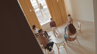 Zihinsel ya da sağlık sorunları olan farklı kişilerin, kadın psikolojisi ile grup terapisi yaptıkları yüksek açılı izleme görüntüleri. Parlak bir odada birlikte oturuyorlar.