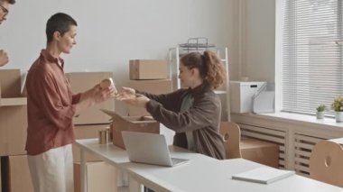 Yardım derneği ofisinde masa başında oturan ve ihtiyaç sahiplerine teneke kutu yiyecek veren cömert genç kadın gönüllülerden oluşan orta boy bir yavaşlama.