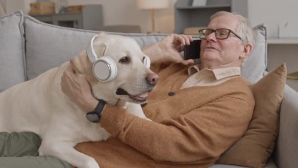 Medium Slowmo Happy Senior Man Talking Phone While Lying Sofa — Vídeos de Stock