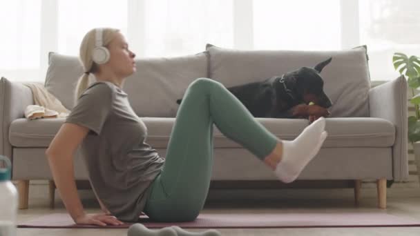 Sarışın Beyaz Kadın Kulaklık Tayt Tişört Giyiyor Oturma Odasında Spor — Stok video
