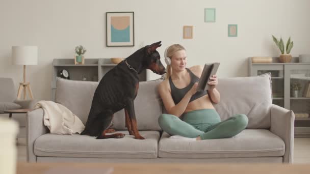 헤드폰 레깅스 스포츠 착용하고 소파에 타블렛 컴퓨터를 사용하는 여성의 — 비디오