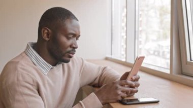 Kafenin önünde oturmuş dijital tablet üzerinde çalışan Afro-Amerikalı ciddi iş adamının yan görüntüsü.