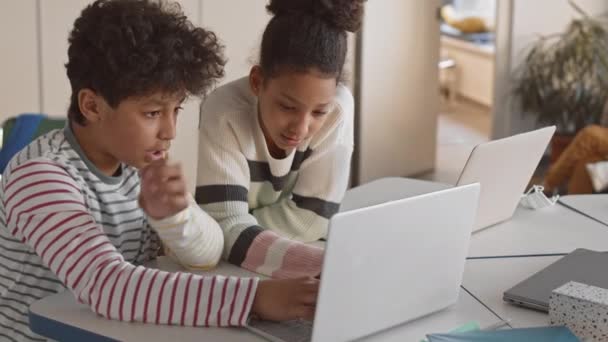 中程度の遅いかわいいアフリカ系アメリカ人の子供たちは 現代の多文化学校でのレッスンの間に休みながらラップトップでゲームをプレイ — ストック動画