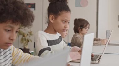 Modern sınıfta bilişim eğitimi alırken sınıf arkadaşının bilgisayarına bakan Afro-Amerikan öğrenci yavaşlığı ile orta boy yakın çekim.