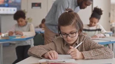 Beyaz tenli, 11 yaşında okul çocuğu sınıfta oturmuş test yapıyor. Genç Afro-Amerikan öğretmen de bir kağıt parçasını göstererek ona yardım ediyor.