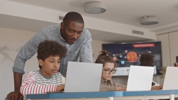 男性の中低速アフリカ系アメリカ人学校教師ノートパソコン画面を見て彼の才能の作品を制御するItのレッスンで5年生の混合レース学生 — ストック動画