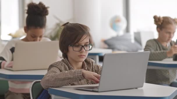 机の上に一人ずつ座って 現代多文化学校のラップトップやデジタルタブレットで勉強する5 6年生の多民族の学童のPan中低速 — ストック動画