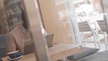 Kafe masasında dizüstü bilgisayarın önünde oturan yatırımcılarla telefonda konuşan ciddi iş adamının orta pencerede çekilmiş resmi.
