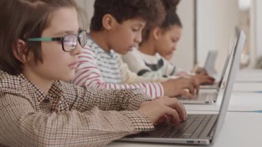 Gözlüklü, zeki, beyaz okul öğrencisinin diğer sınıf arkadaşlarıyla birlikte ders çalıştığı yakın plan çekimler.