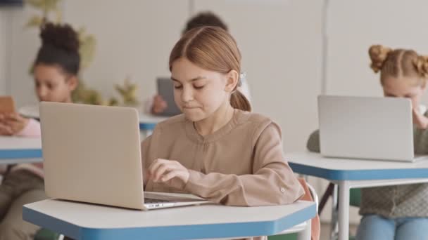 中程度の遅いのスマート白人女子高生の5または6年生座ってデスクで多文化授業勉強のラップトップ — ストック動画