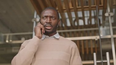 Genç, yakışıklı, Afro-Amerikan iş adamının dışarıda telefon görüşmesi yaparken orta açıdan çekilmiş bir fotoğrafı.