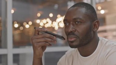 Vahşi Afro-Amerikan bir adamın hoparlörle telefon edip kahve içerek kafenin önünde oturması.