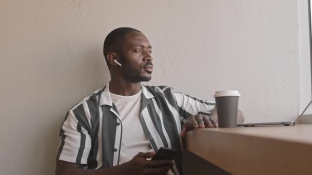穿着便服和耳塞的现代非洲裔美国人在舒适的咖啡店边听着音乐边看窗户边听着咖啡 — 图库视频影像