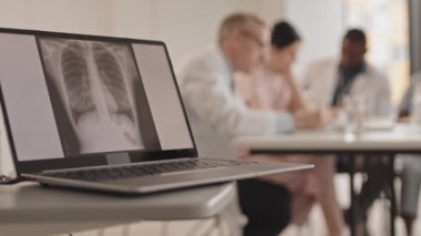 Göğüs röntgeni ve bulanık arkaplandaki teşhisi tartışan doktorlarla dizüstü bilgisayarın yakın plan görüntüsü.