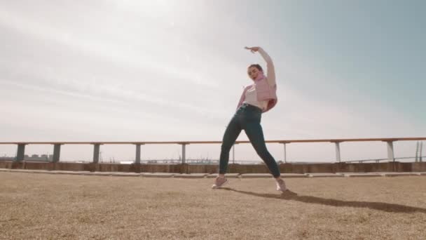 年轻健康的白人女子穿着牛仔裤和宽松背心 在城市路堤上跳现代舞步的全景 — 图库视频影像