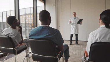 Tıp konferansı ya da seminer sırasında meslektaşlarının konuşma yapmasını dinleyen küçük çok ırklı doktorların dikiz görüşü yavaşlıyor.