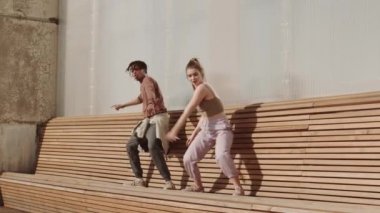 Genç, Afrikalı bir adam ve beyaz bir kadının uzun tahta bankta dans ederken geniş açılı görüntüsü.