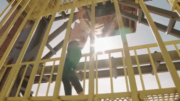 穿着牛仔裤和宽松夹克的快乐的高加索女人的低角度Pov 在楼梯上用黄色工业金属栅栏表演现代舞步 — 图库视频影像