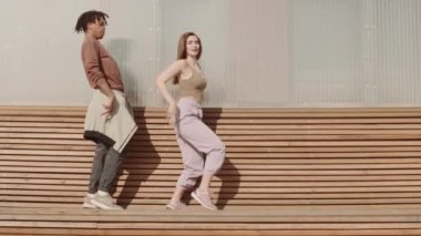 Genç Afrikalı bir adam ve beyaz bir kadının uzun tahta bankta dans ederken geniş açılı görüntüsü.