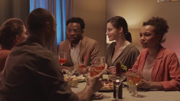家でお祝いのディナーテーブルに座って会話をしている若い多民族のグループのスローショット — ストック動画