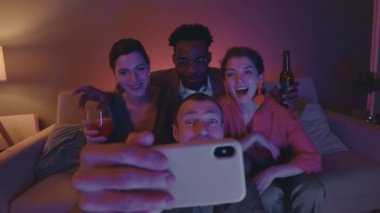Neşeli bir grup arkadaşın ev partisinde kameraya gülüp komik surat ifadeleri takınarak akıllı telefonlarda selfie çekerken yavaş çekimleri.