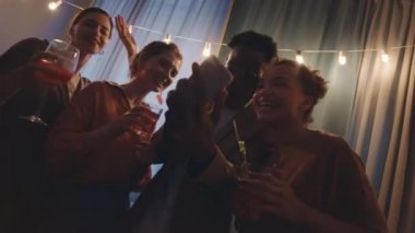 Partide birlikte dans eden beş neşeli kadın ve erkeğin yavaşlaması kendilerini videoya kaydetmek ya da aydınlatma ile birlikte parti yaparken akıllı telefondan video araması yapmak.