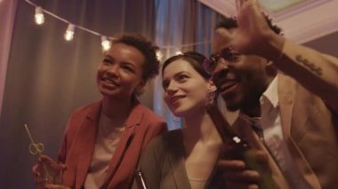 İki genç kadın ve Afrikalı-Amerikalı adamın düşük açılı yavaşlığı ev partisinde arkadaşlarıyla video konferansı yapıyor.