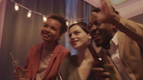 2人の若い女性とアフリカ系アメリカ人の男のビデオ会議の低角度腰アップのスローモ一緒に楽しみを持っているパーティー中に彼らの友人と — ストック動画