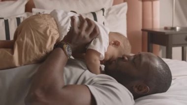 Gururlu, genç Afrikalı bir adam yatakta yatıyor, tapılası bebeğini elinde tutuyor, onu yukarı kaldırıyor, babasının gülümseyip oğlunu öpüyor.