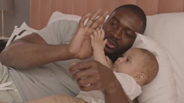 Orta yaşlı, gururlu Afrikalı bir adam, yeni yürümeye başlayan çocuğuyla yatakta yatıyor, babasının eliyle oynuyor, beşlik çakıyor.
