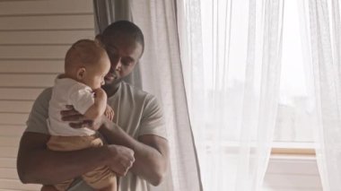 Genç, mutlu bir babanın küçük oğlunu kucaklaması, ona hayran olması, öpücükler vermesi, pencerenin önünde durması.