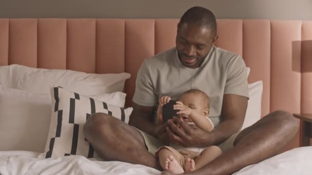 Tiro Completo Joven Africano Feliz Sentado Cama Mostrando Teléfono Inteligente — Vídeo de stock