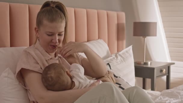 中年白种人年轻而快乐的女人坐在床上 给婴儿喂奶 微笑着 — 图库视频影像