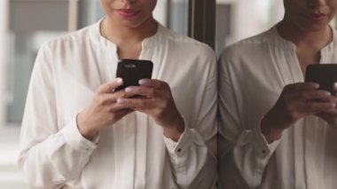 Gözlüklü, kendine güveni tam bir iş kadını görüntüsü ve modern ofis binasının cam duvarına yansıyan akıllı telefondan sarkan akıllı bir giysi.