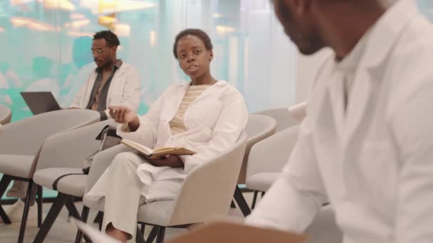 現代の大学教室での講義やセミナーで男性教授と会話をしながら白いコートを着た若い女性アフリカ系アメリカ人医療学生の中程度のショット — ストック動画