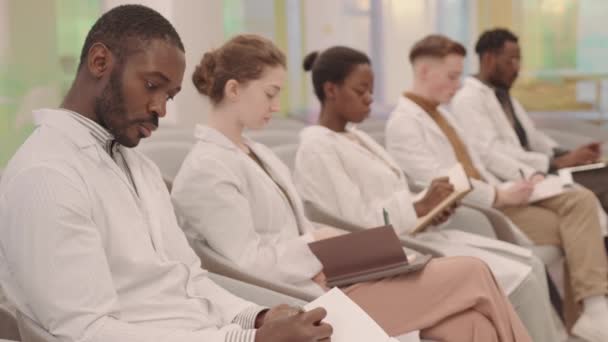 当代课堂上一排排身穿白衣 听讲座 记笔记的年轻多民族医学生侧视图 — 图库视频影像