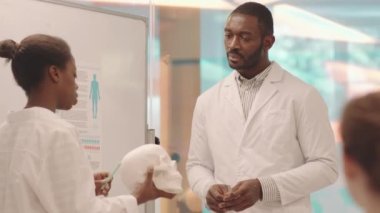 Beyaz önlüklü Afro-Amerikan genç tıp öğrencisi ve üniversite profesörü Anatomi dersinde insan beyni kafatası modeliyle beyaz önlüklü.
