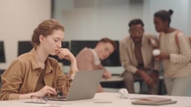 Sınıftaki kız öğrencinin laptopta çalışırken, sınıf arkadaşlarının buruşuk kağıt parçalarını fırlattığı orta boy bir fotoğraf.