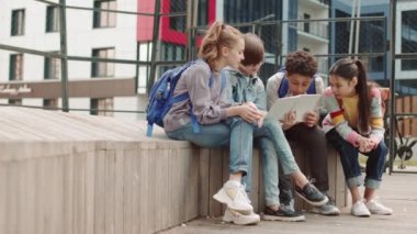 Bir grup liseli çocuğun yazın çocuk parkındaki bankta oturup kitap okurken sohbet etmelerinin yavaş çekimi.