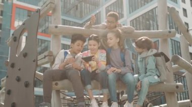 Çocuk parkında akıllı telefondan oyun oynayan neşeli çoklu etnik gruptan düşük açılı yavaş çekim.