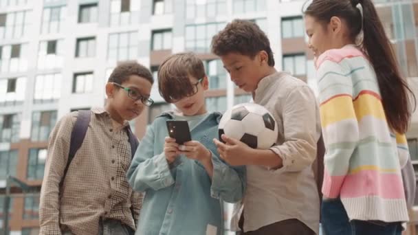 遊び場でスマートフォンを使用している間に楽しんでいる異なる民族の未成年の子供たちのグループの低角度中ショット — ストック動画