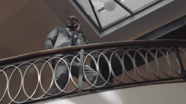 Düşük açılı orta ölçekli başarılı Afro-Amerikan CEO özel yapım takım elbise giyiyor, cep telefonuyla merdivenlerde konuşuyor.