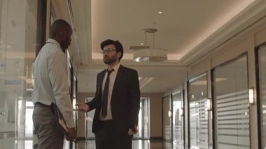 Formalite icabı giyinen, sohbet eden, koridorda dikilen iki genç erkek arkadaşın orta uzunlukta olduğu bir yer.