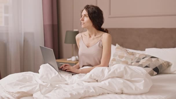 캅카스 여성들 침대에 노트북 컴퓨터로 타자를 컴퓨터를 웃으며 일어나고 있습니다 — 비디오